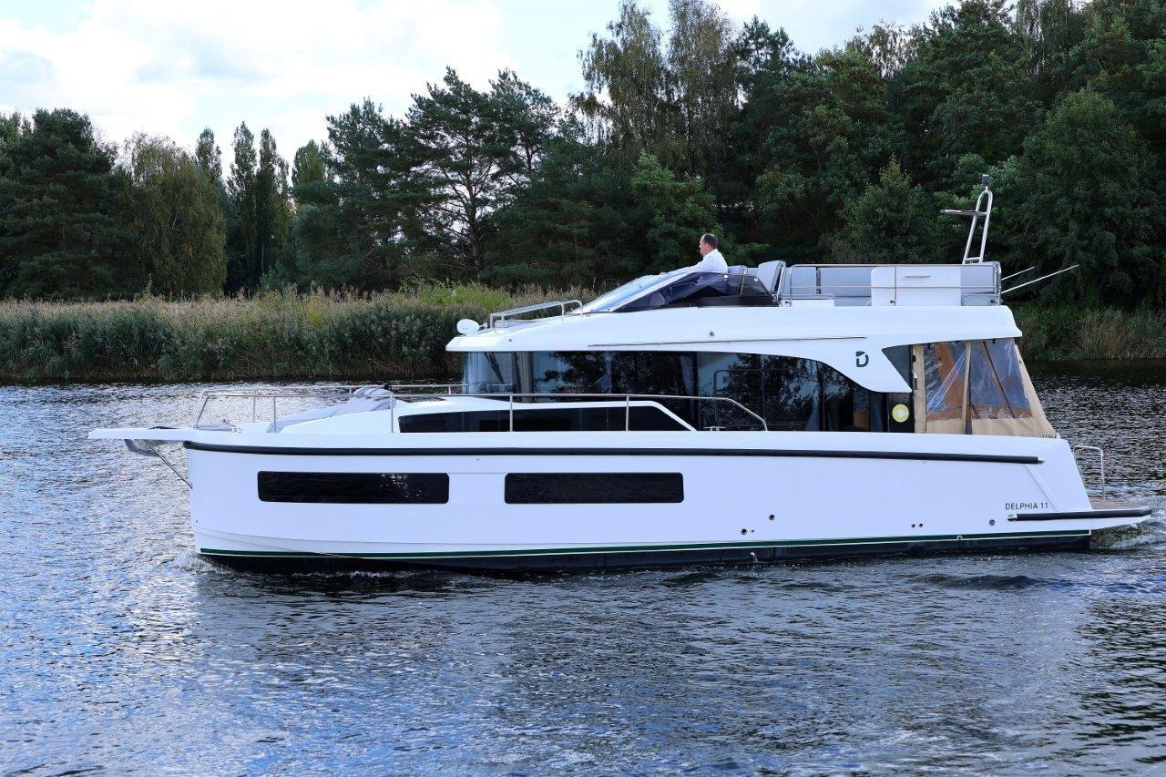 2023 Delphia 11 Flylounge yacht cruising on a serene lake with lush greenery.