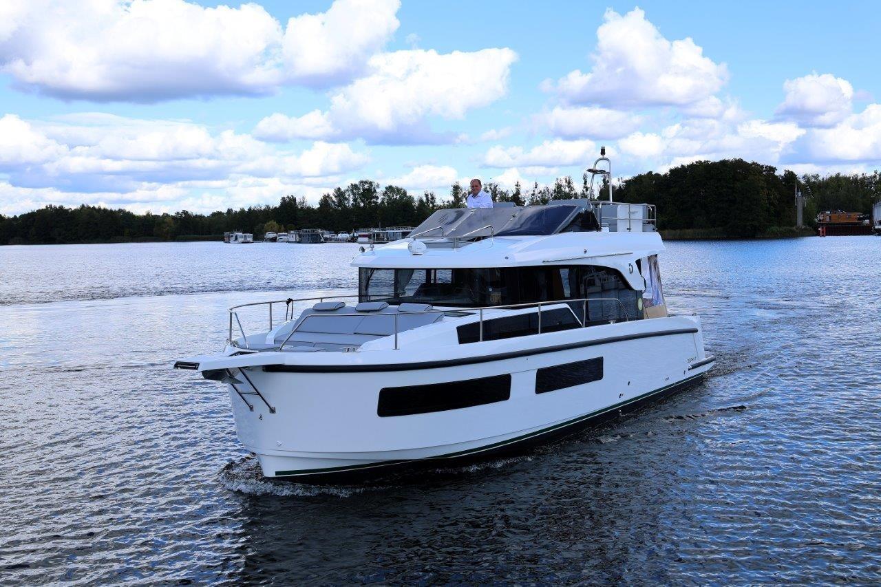 2023 Delphia 11 Flylounge yacht cruising on a serene lake under a cloudy sky.