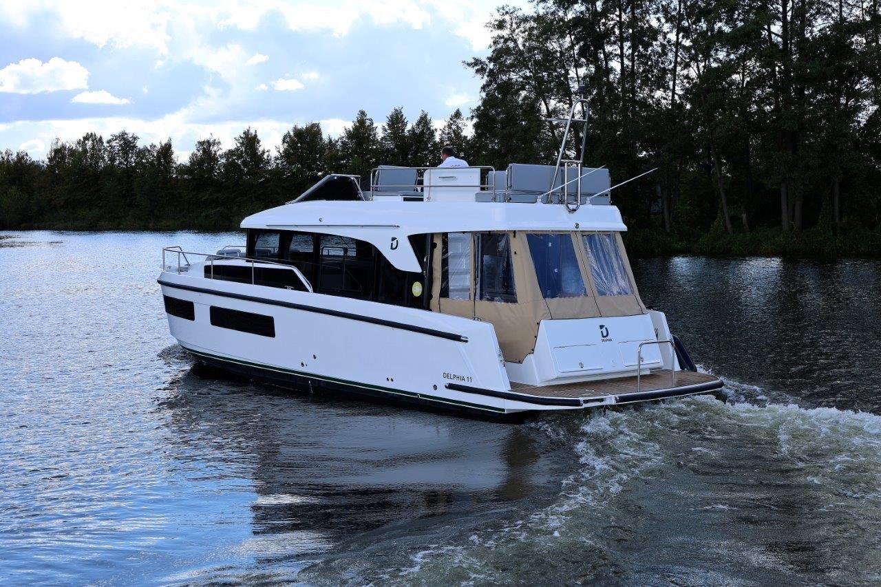 2023 Delphia 11 Flylounge cruising on a serene lake with lush trees in the background.