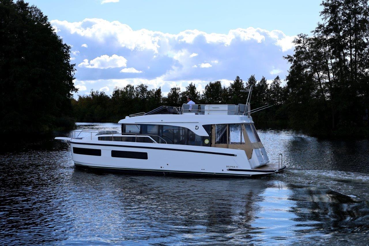 2023 Delphia 11 Flylounge cruising on a serene lake with lush trees and blue sky.