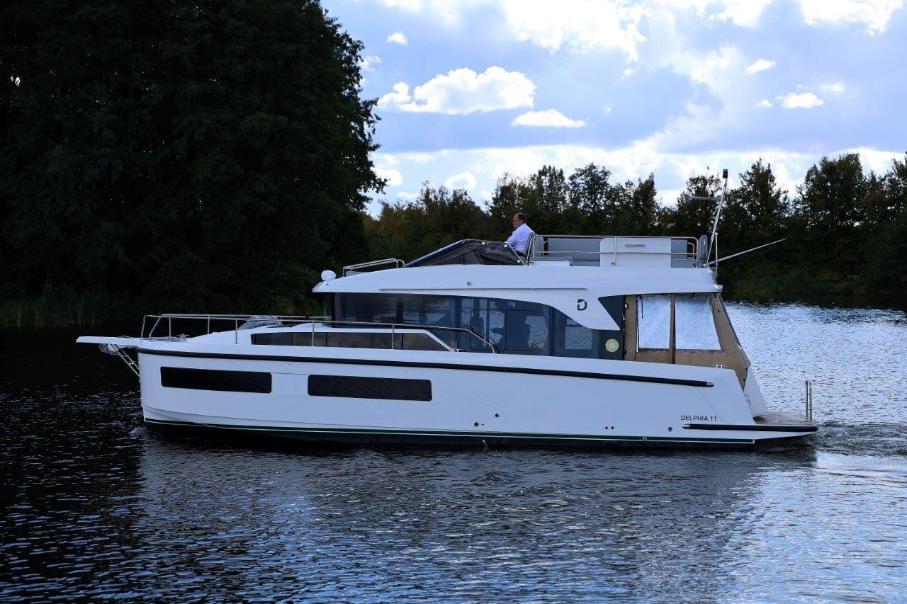 2023 Delphia 11 Flylounge yacht cruising on a serene lake under a partly cloudy sky.