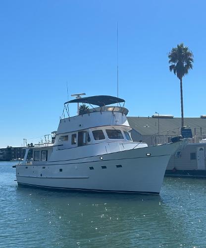 1977 Grand Alaskan Raised Pilothouse yacht on calm water, sunny day, palm tree in background.