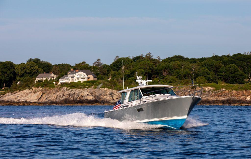 2026 Sabre 43 Salon Express cruising near rocky shoreline with houses in the background.