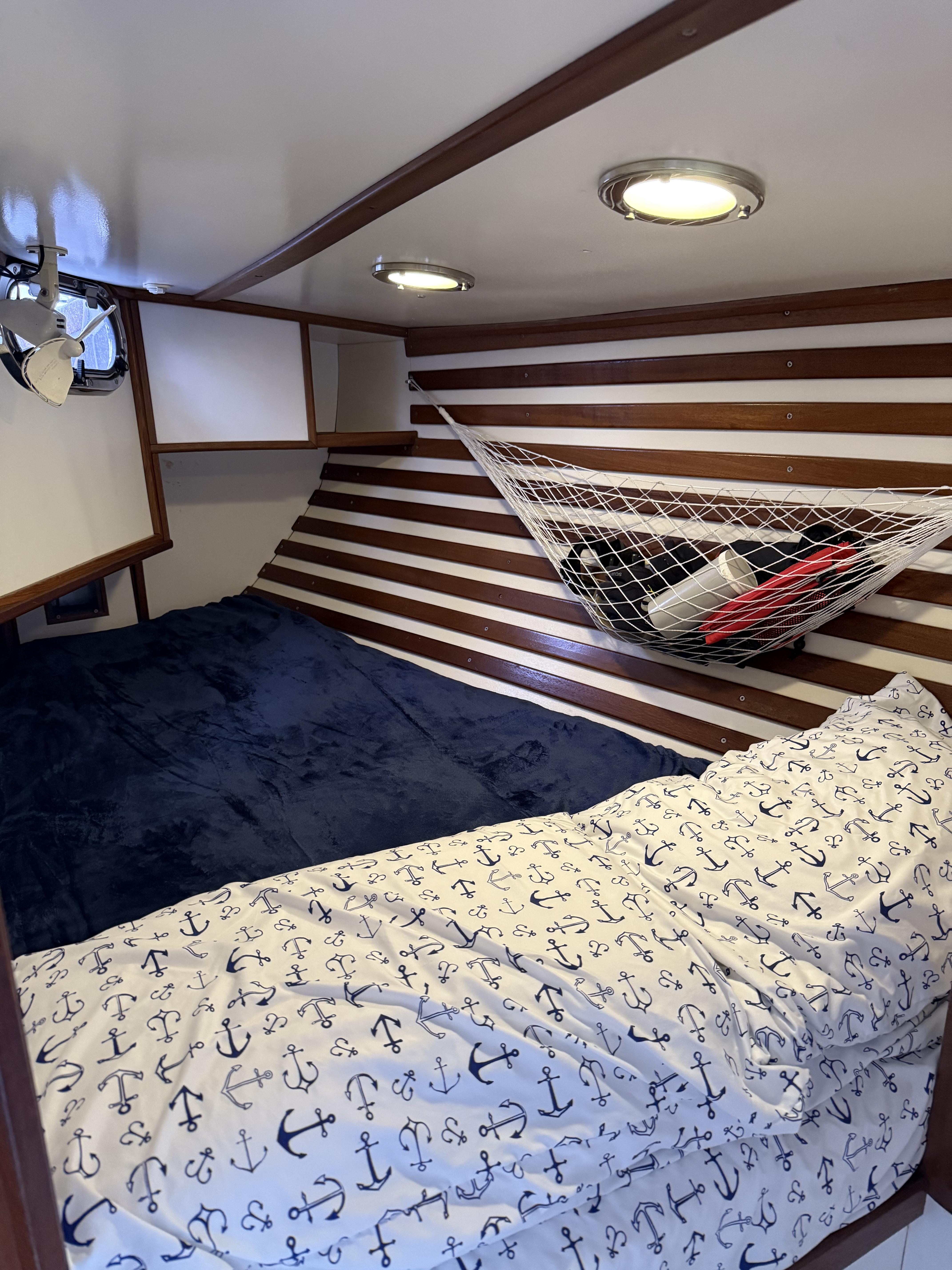 Cozy cabin interior of 1976 Frers Custom boat with nautical-themed bedding and storage hammock.