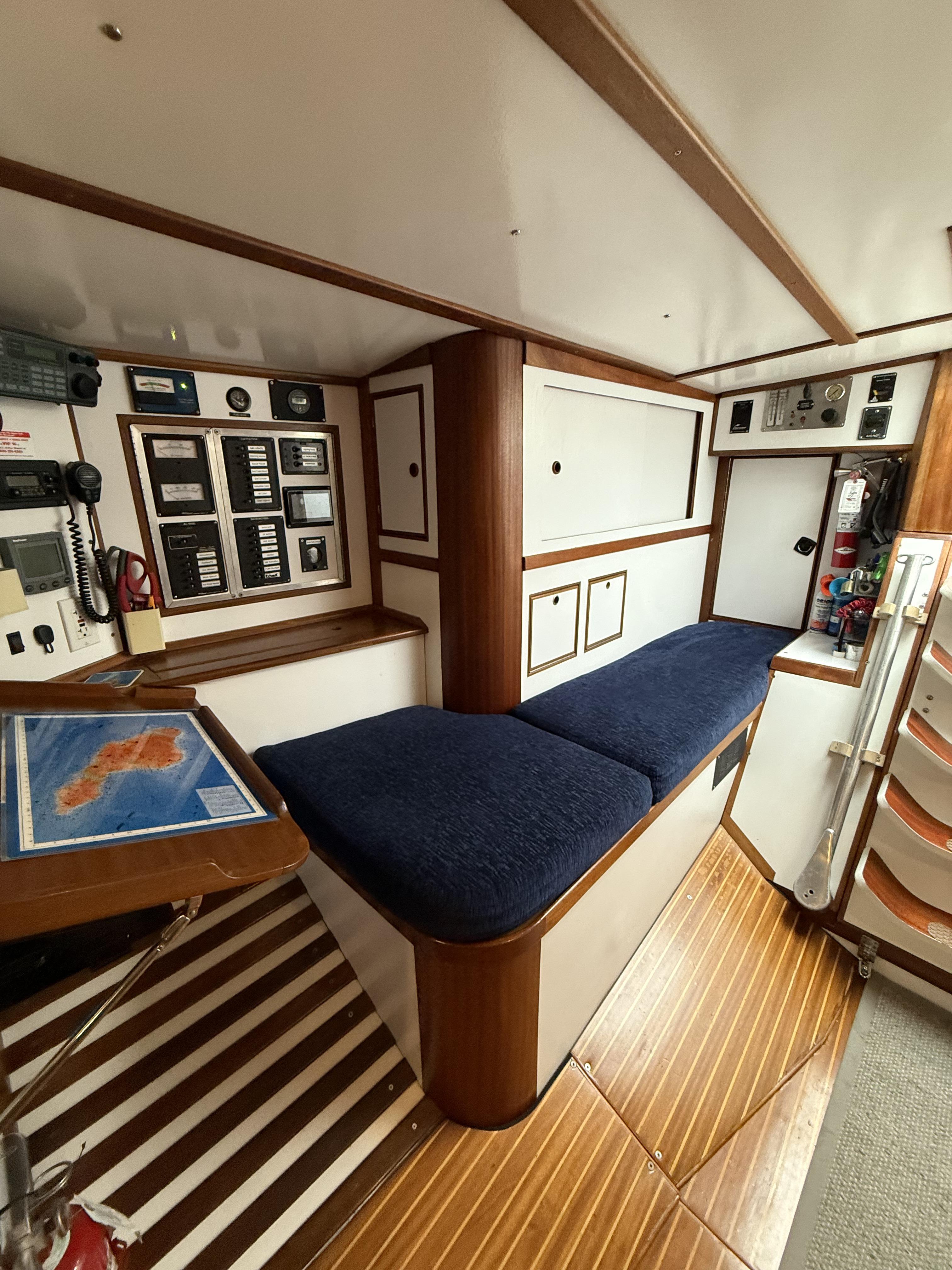 1976 Frers Custom yacht interior with navigation station, blue cushioned seating, and wooden flooring.