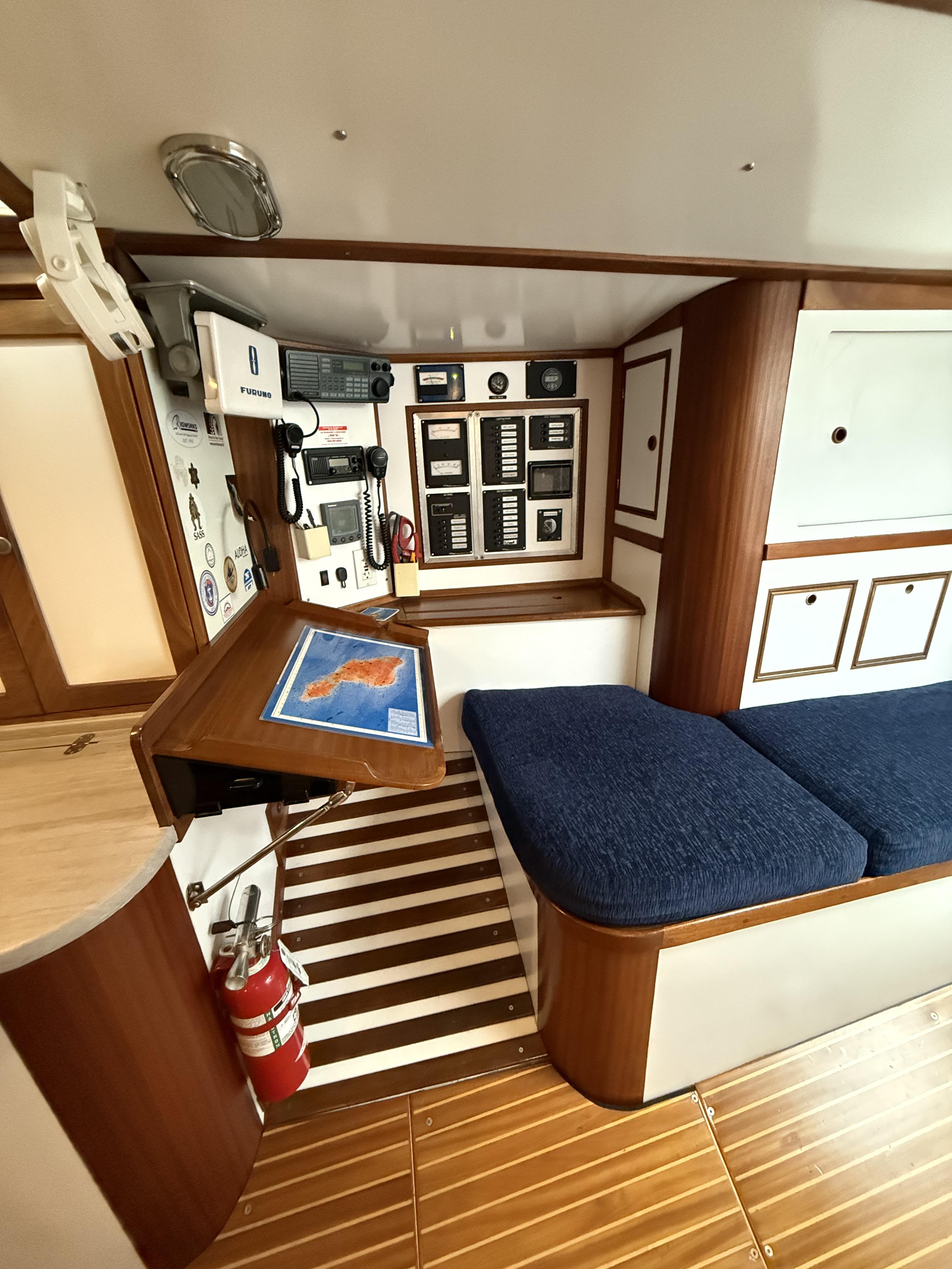 Interior of 1976 Frers Custom yacht with navigation station and blue cushioned seating.