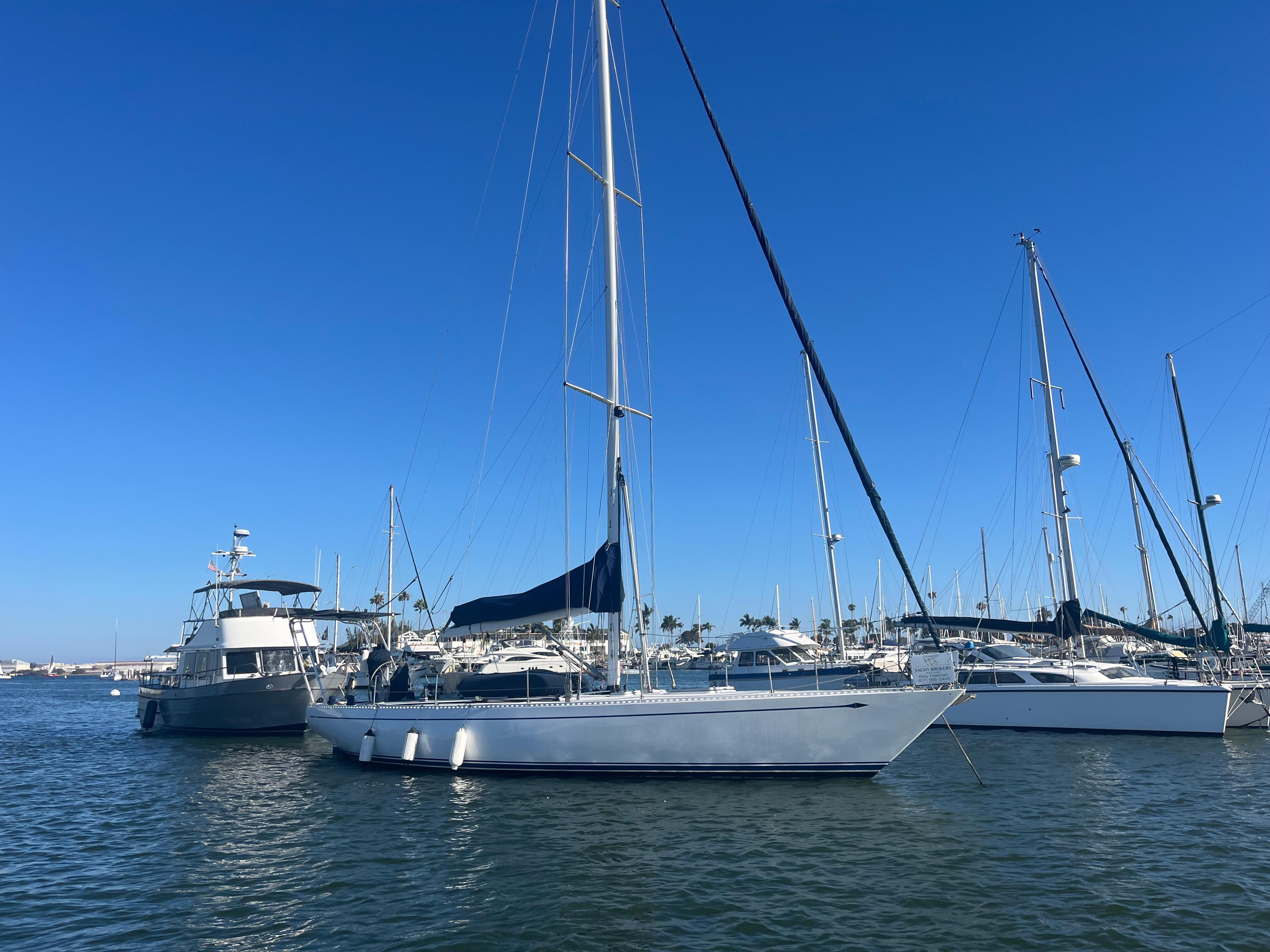Sailboats docked in a marina under clear blue skies, featuring a 1976 Frers Custom model.