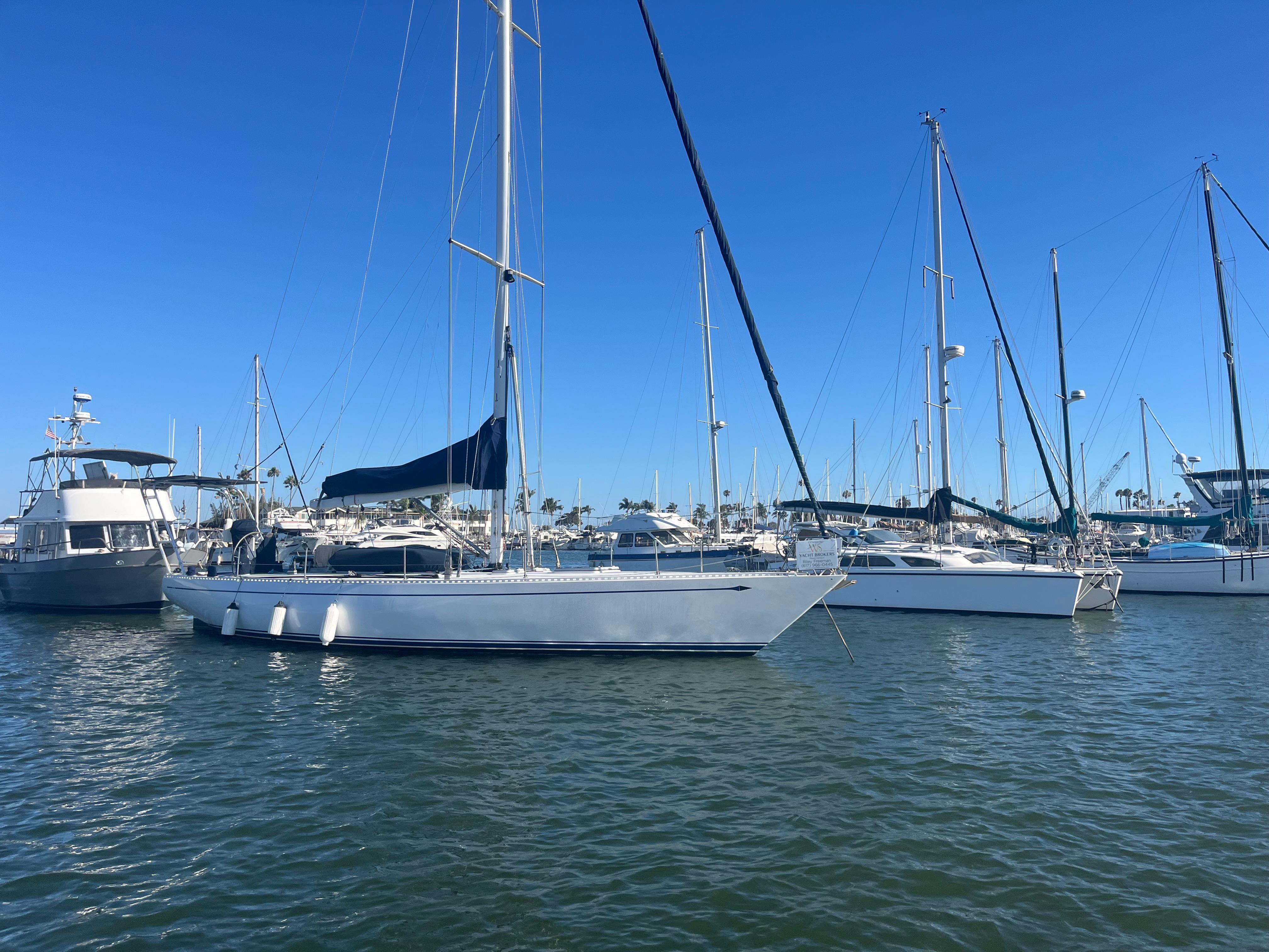 Sailboats docked in a marina, featuring a 1976 Frers Custom model under clear blue skies.