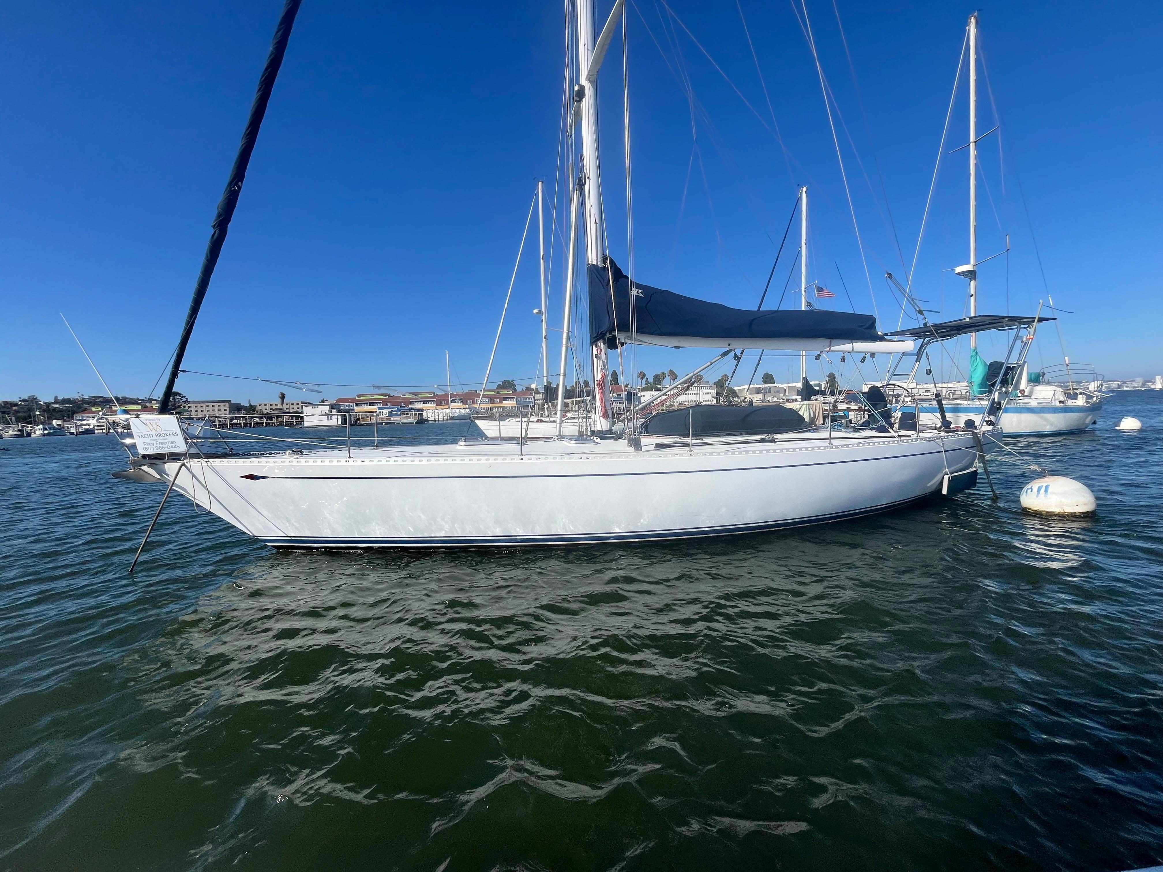 1976 Frers Custom sailboat on calm water, clear blue sky background.