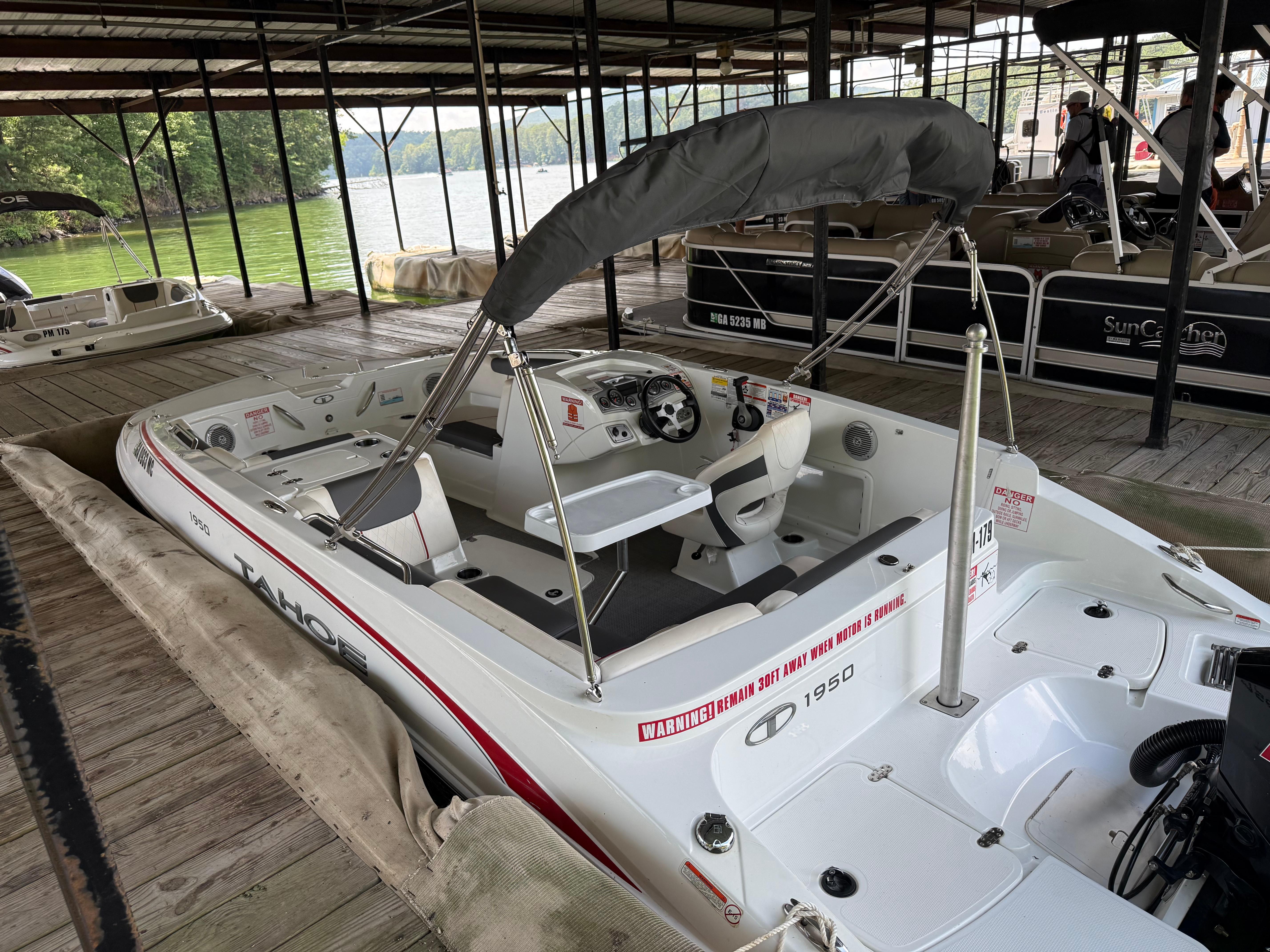Tahoe 1950 boat docked, 2021 model, with canopy and steering wheel, at a lakeside marina.