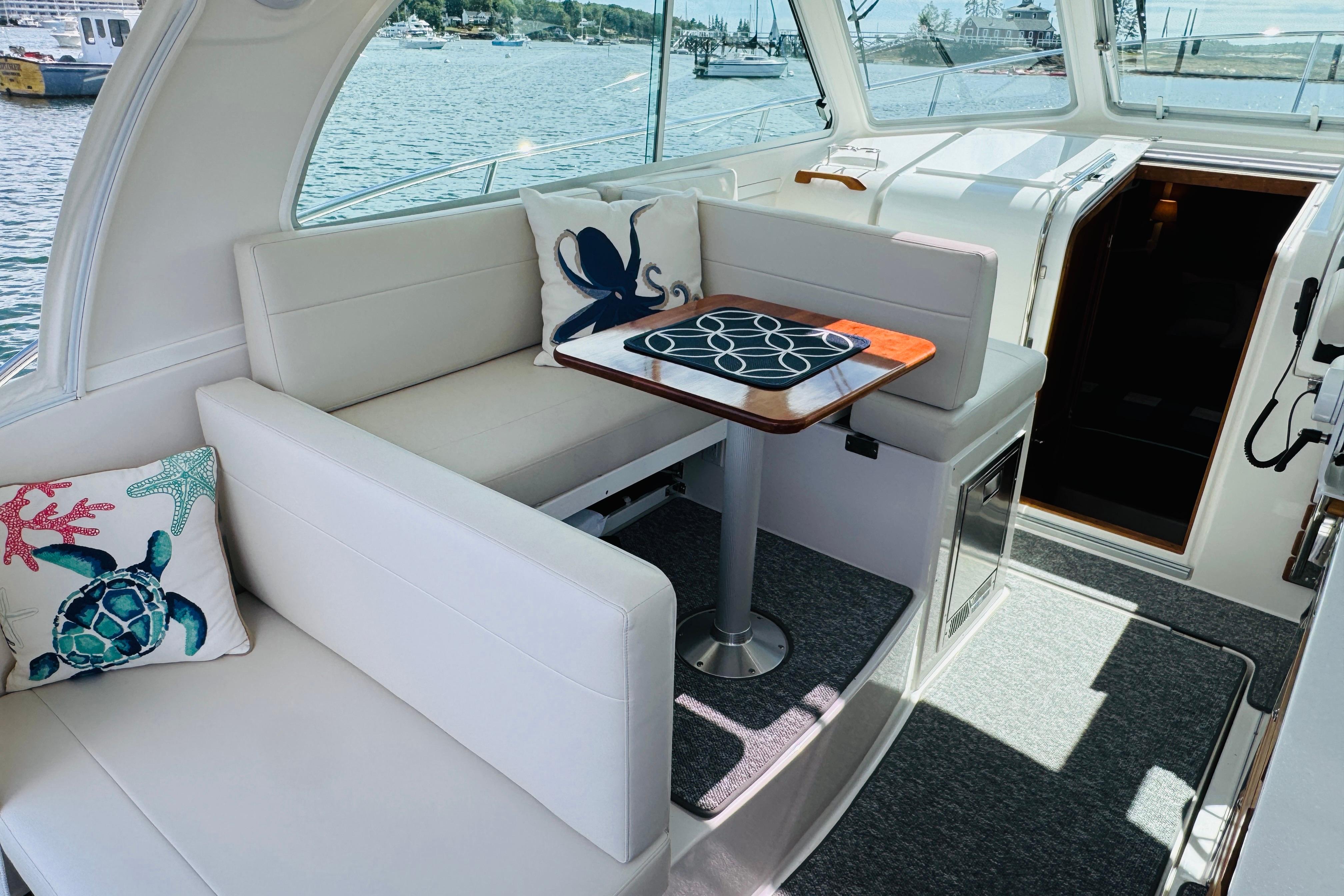 2025 Back Cove 34O boat interior with plush seating, nautical-themed pillows, and a wooden table.