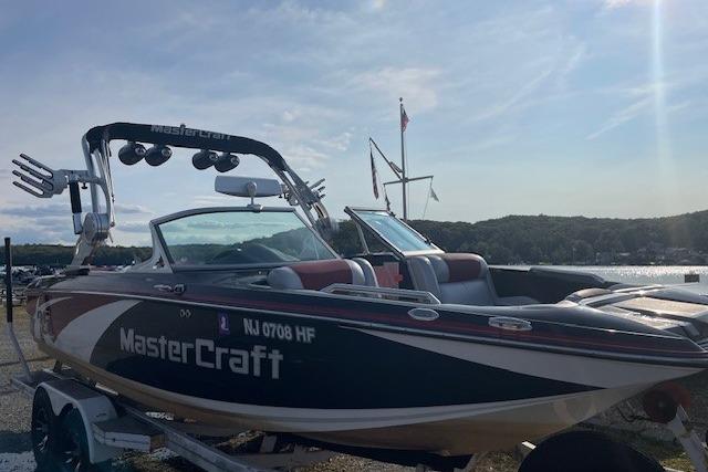 2013 MasterCraft X-25 boat on trailer by a lake under a clear sky.