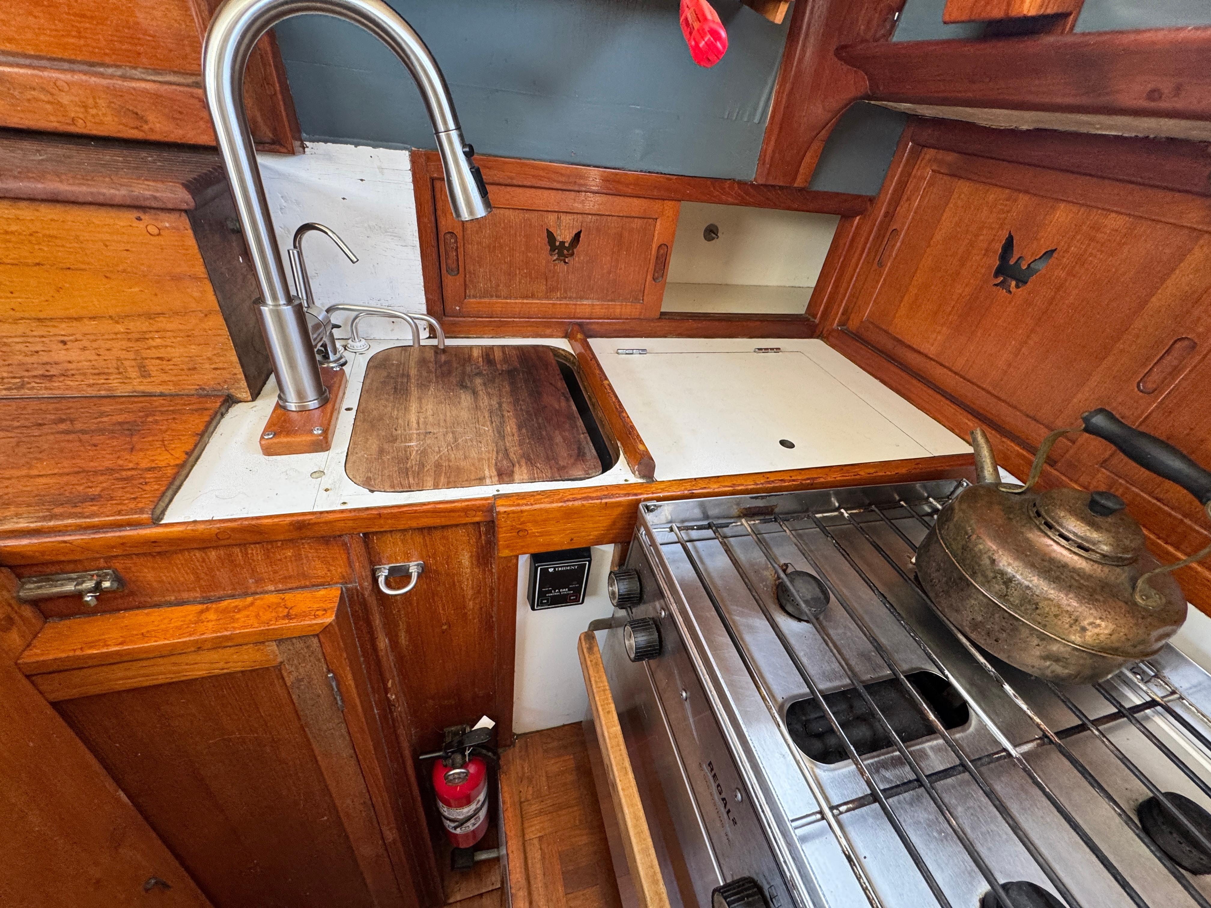 1970 Cheoy Lee Luders 36 yacht kitchen with wooden cabinetry and stainless steel sink.