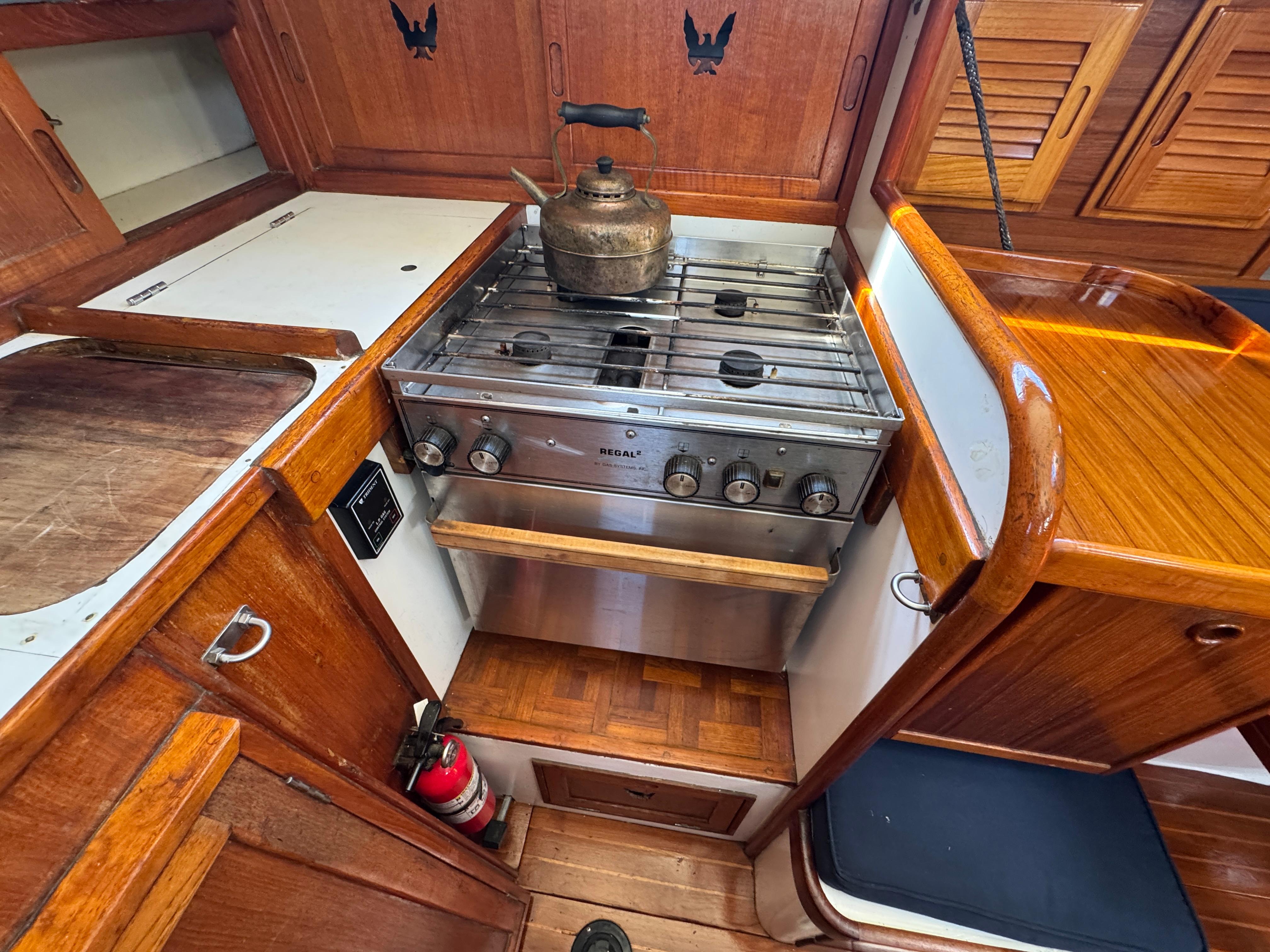1970 Cheoy Lee Luders 36 yacht kitchen with stove, kettle, and wooden cabinetry.