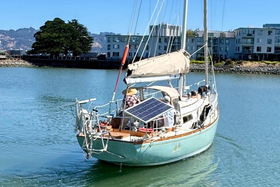 1970 Cheoy Lee Luders 36 sailboat with solar panel, cruising near waterfront buildings.