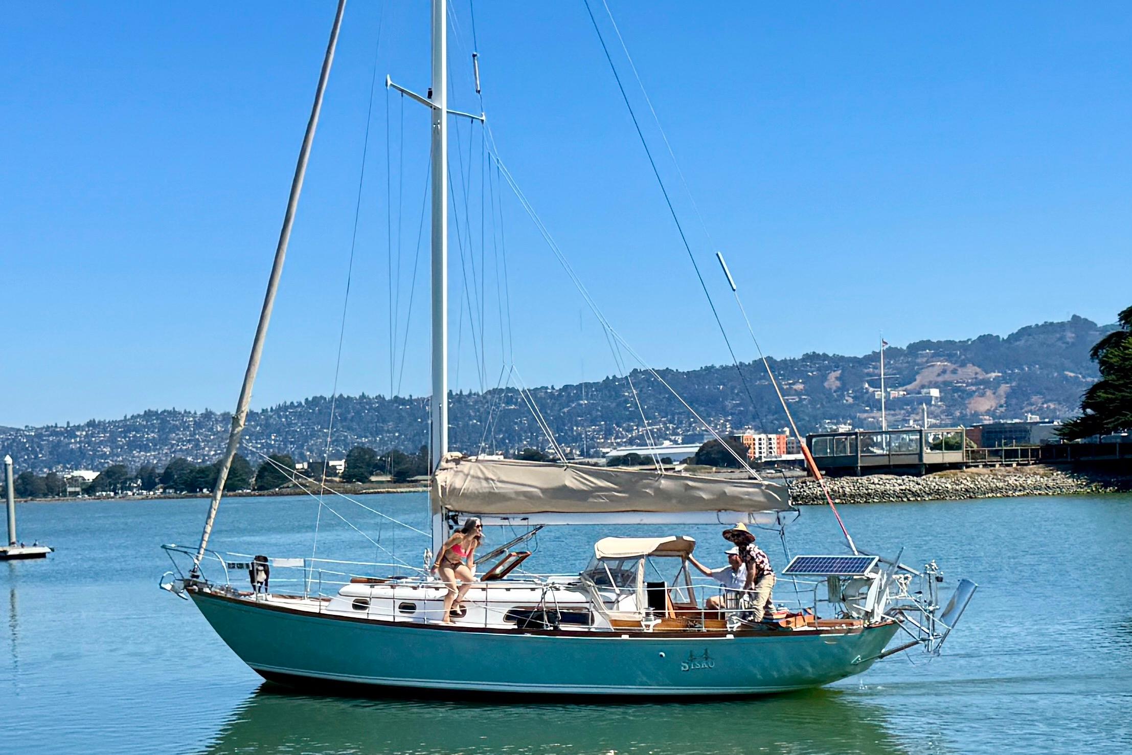 1970 Cheoy Lee Luders 36 sailboat on calm water, with scenic mountain backdrop.