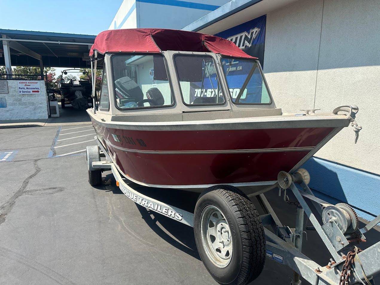 2003 Alumaweld Stryker boat with red canopy on trailer, parked outside a building.