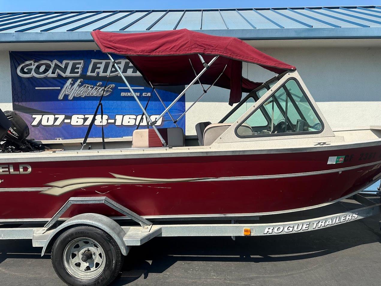 2003 Alumaweld Stryker boat with maroon canopy on Rogue trailer, parked outside.