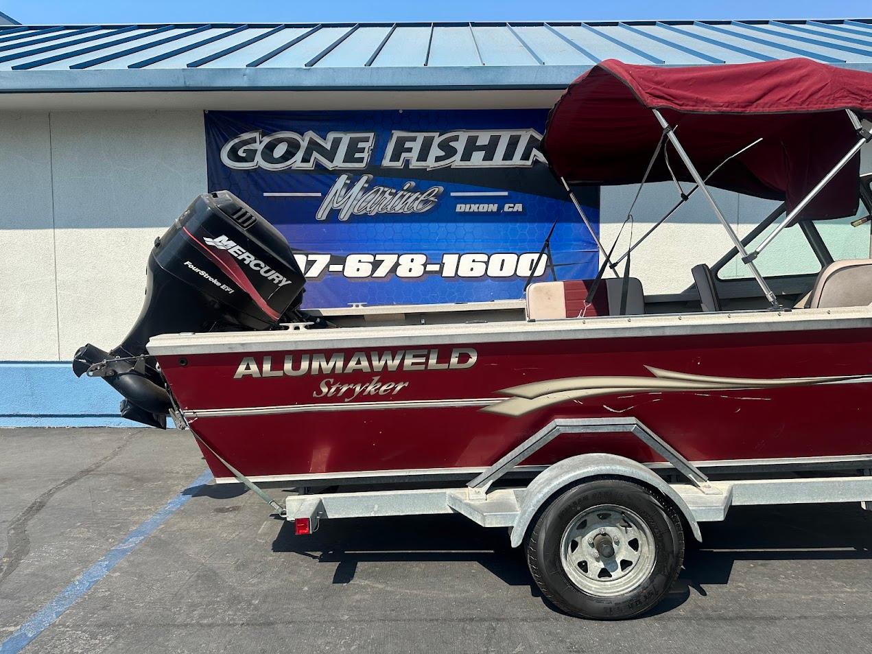 2003 Alumaweld Stryker boat with Mercury engine, parked outside a marine shop.