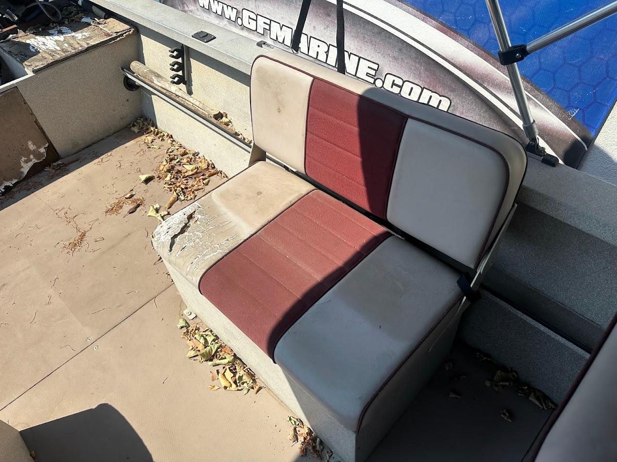 Worn seating on 2003 Alumaweld Stryker boat, surrounded by fallen leaves and debris.