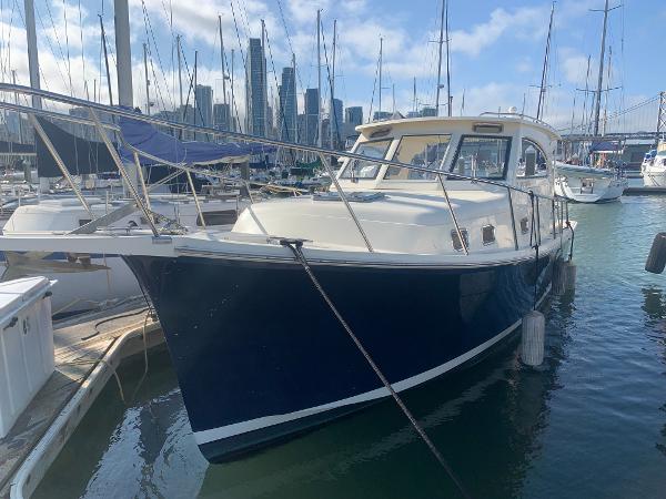 2004 Mainship Pilot 30-II Sedan docked in marina with city skyline background.