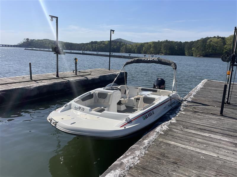A 2021 Tahoe 1950 boat docked on a serene lake with wooded shoreline.