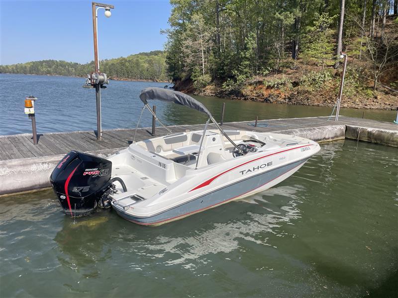 2021 Tahoe 1950 boat docked on a serene lake with lush green surroundings.