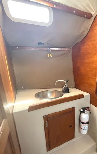 1979 Lancer Sloop interior with sink, wooden cabinet, and fire extinguisher.