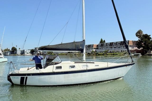 1979 Lancer Sloop sailboat on calm water with a person onboard, near residential area.