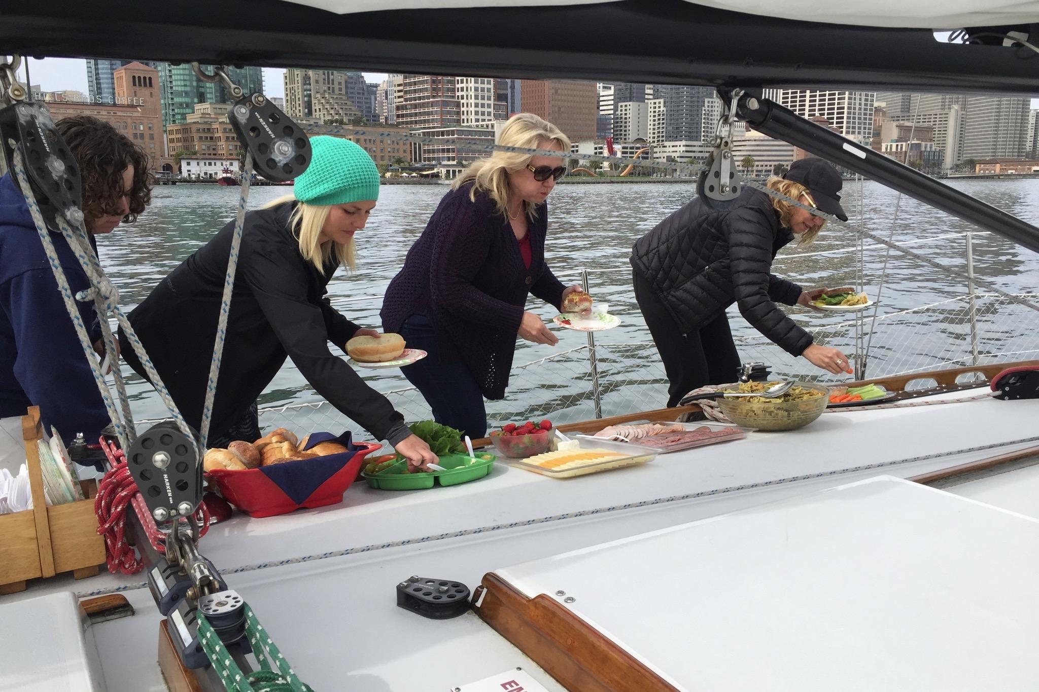 People enjoying a meal on a 1982 Santa Cruz 50 sailboat in a city harbor.