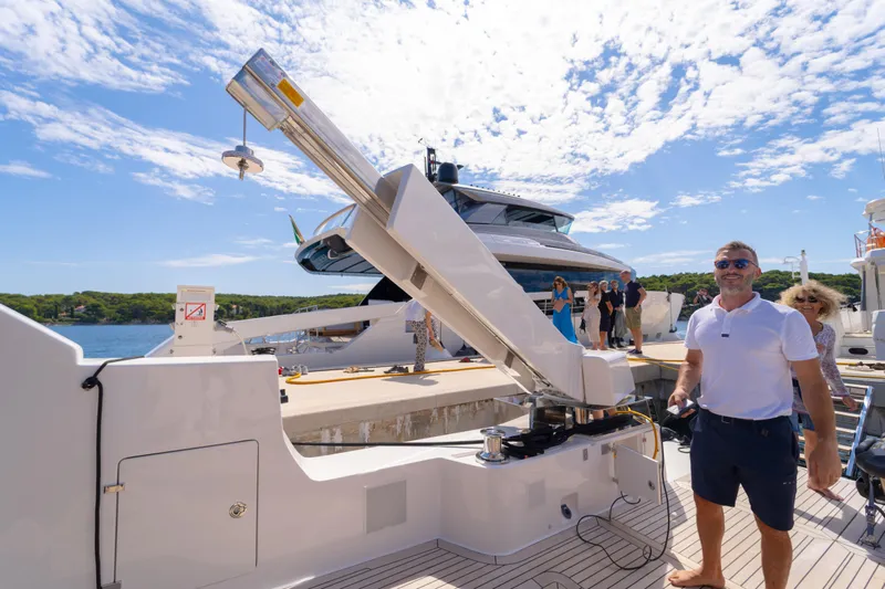  Yacht Photos Pics Man on Bluegame BG74 yacht, 2025 model, docked with people in the background under a sunny sky.