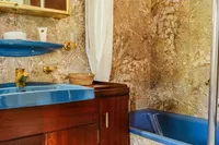 Vintage 1982 bathroom with blue fixtures, marble walls, and wooden cabinetry on a custom vessel.