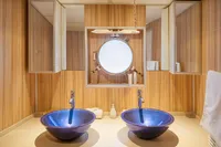Luxurious bathroom with twin blue vessel sinks, wooden paneling, and a round mirror.