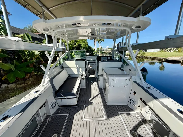  Yacht Photos Pics 2019 Blackfin 272 DC boat interior with seating, storage, and helm, docked by lush greenery.