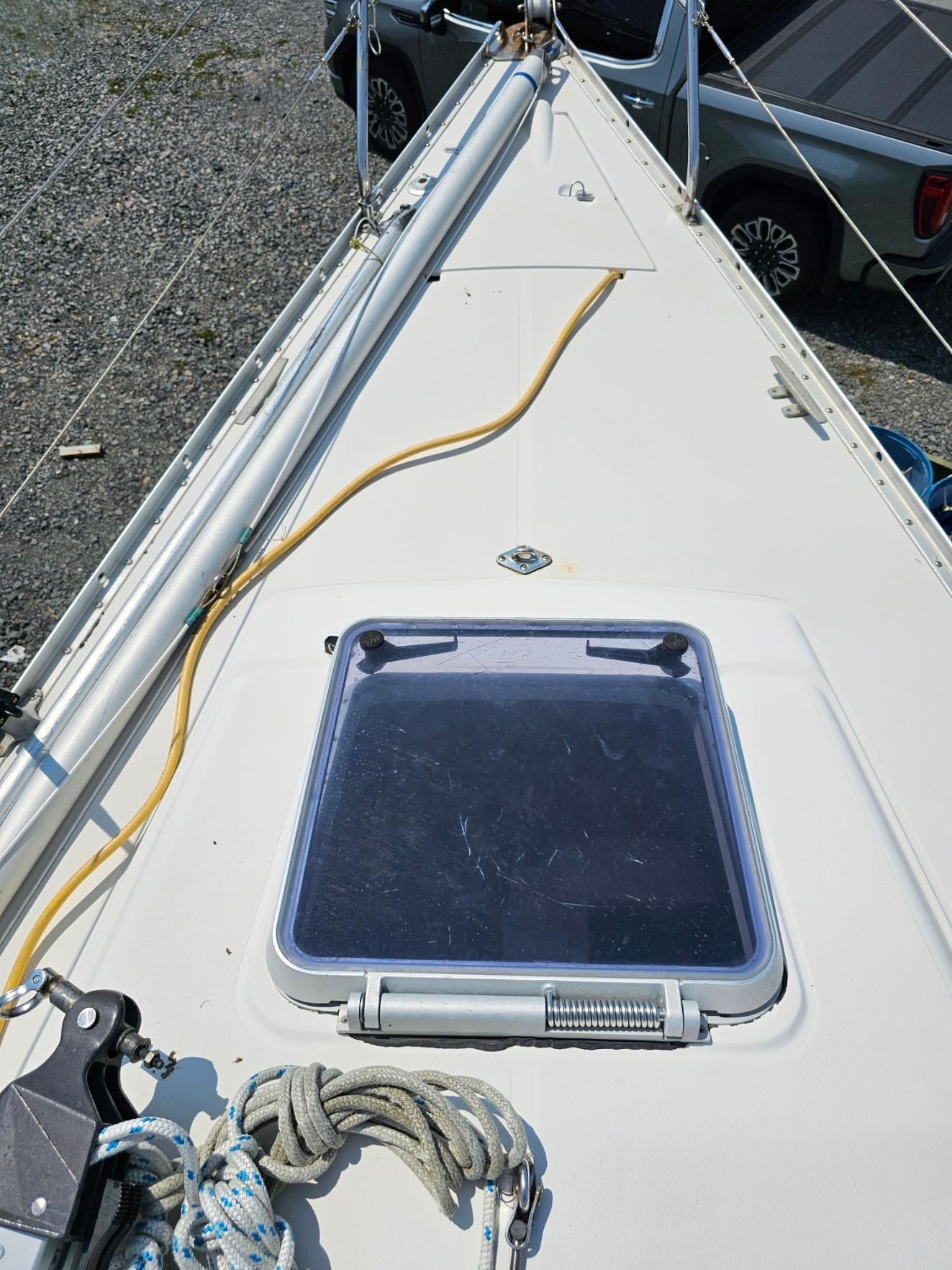 1987 CS 30 sailboat deck with hatch, ropes, and parked vehicle in background.