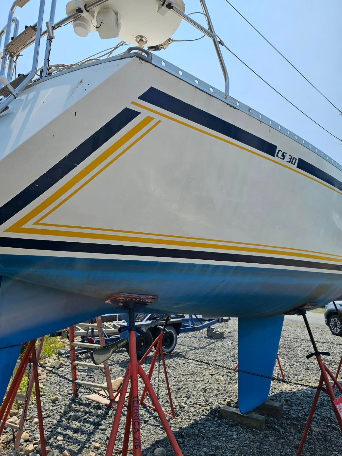 1987 CS 30 sailboat on stands, featuring blue and yellow stripes.