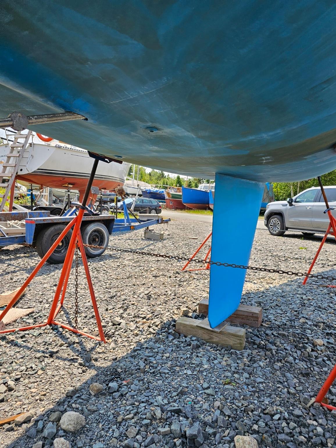 1987 CS 30 sailboat on stands in a boatyard, gravel ground, sunny day.