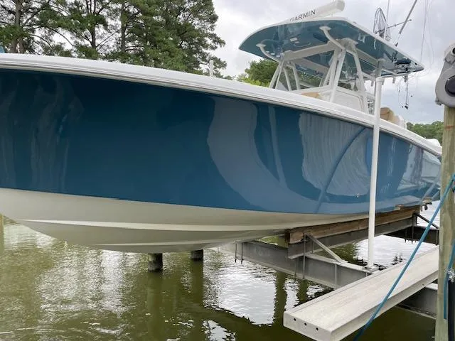  Yacht Photos Pics 2022 Invincible 36 Open Fisherman boat on lift, blue hull, docked by trees.