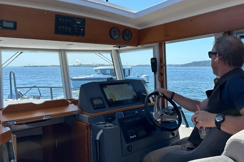 Sisu Yacht Photos Pics Man steering 2020 Sargo 31 boat on a sunny day, with scenic water view.