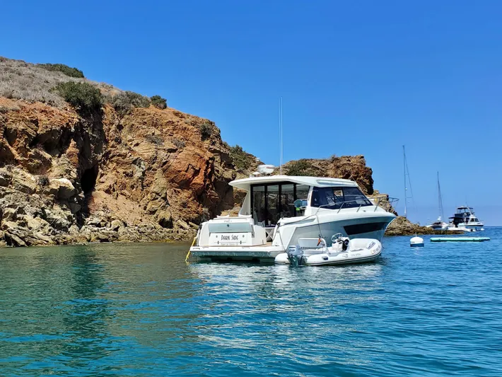 Dark Side Yacht Photos Pics 2017 Jeanneau NC11 yacht anchored near rocky coastline under clear blue sky.