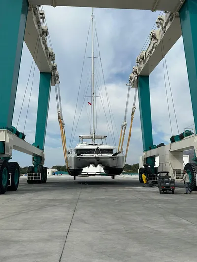  Yacht Photos Pics 2023 Lagoon 55 catamaran being lifted by a large boat hoist at a marina.