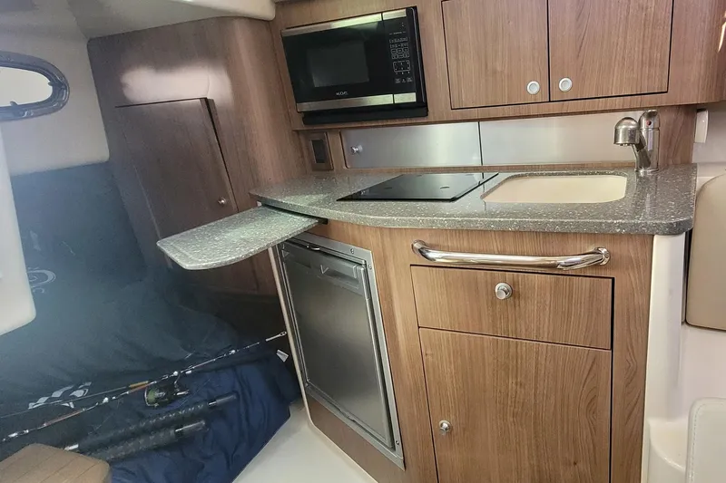 Outta Line Yacht Photos Pics 2017 Boston Whaler 315 Conquest cabin kitchen with wood cabinetry, microwave, and compact appliances.