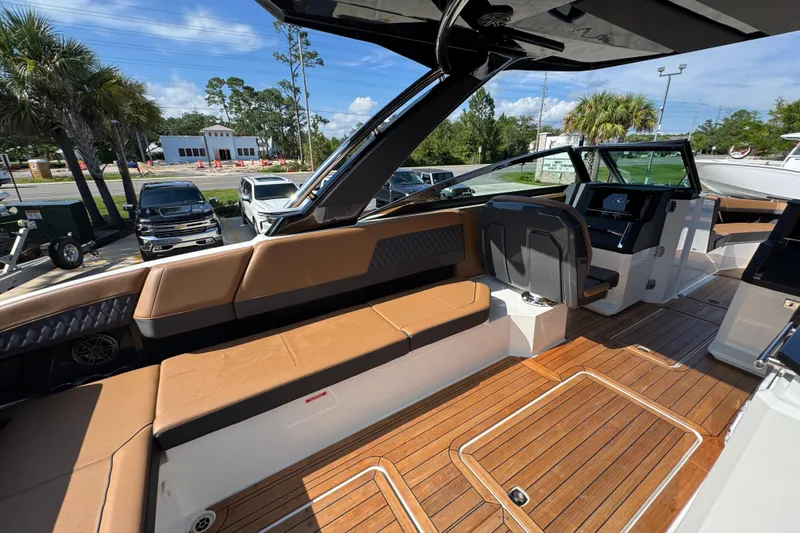  Yacht Photos Pics 2024 Cobalt R33 boat interior with tan seating and wooden flooring, parked outdoors.
