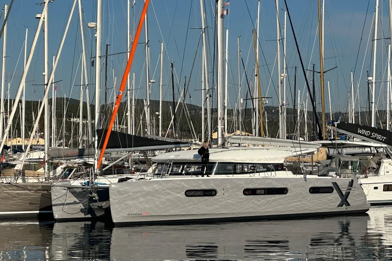  Yacht Photos Pics 2023 CNB EXCESS 15 catamaran docked in a marina, surrounded by sailboats.