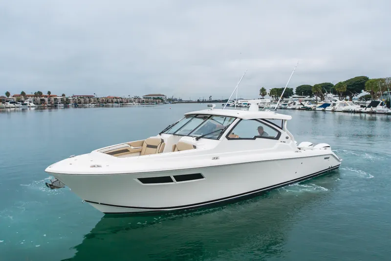  Yacht Photos Pics 2018 Pursuit boat cruising in a marina, surrounded by calm waters and docked yachts.
