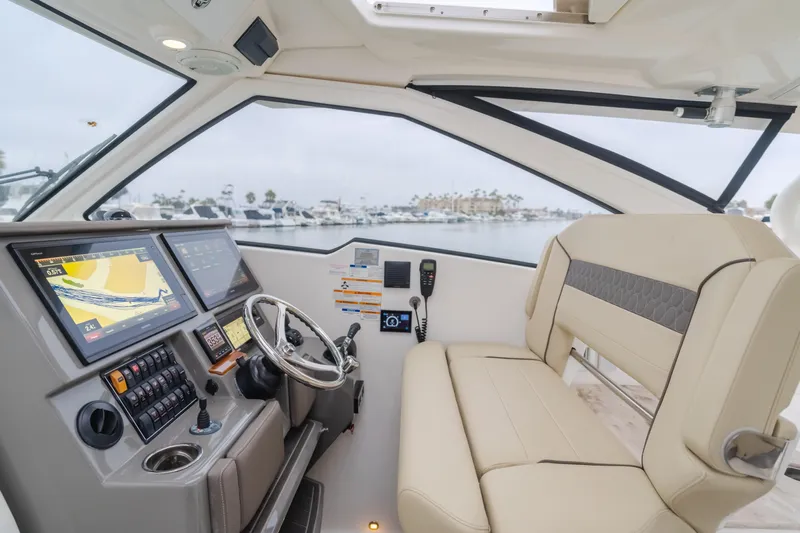  Yacht Photos Pics 2018 Pursuit boat interior with navigation screens, steering wheel, and beige seating.