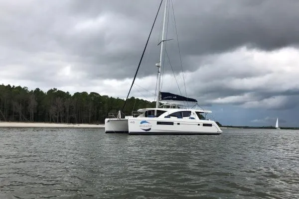 Pilar Yacht Photos Pics 2015 Robertson & Caine Leopard 48 catamaran sailing near a forested shoreline under cloudy skies.