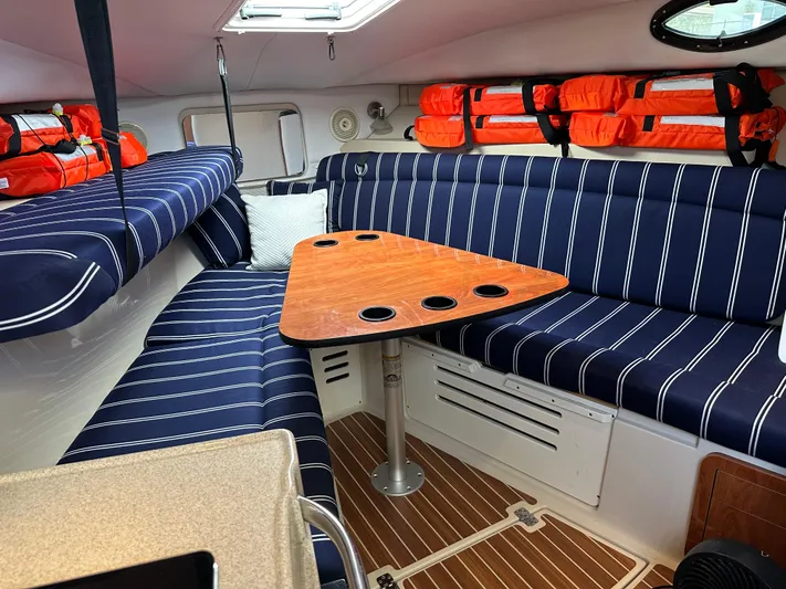 Last One II Yacht Photos Pics 2015 Wellcraft 290 Coastal cabin with striped seating, wooden table, and life jackets.