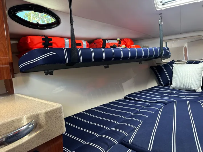 Last One II Yacht Photos Pics 2015 Wellcraft 290 Coastal cabin with striped bedding and life jackets on shelf.