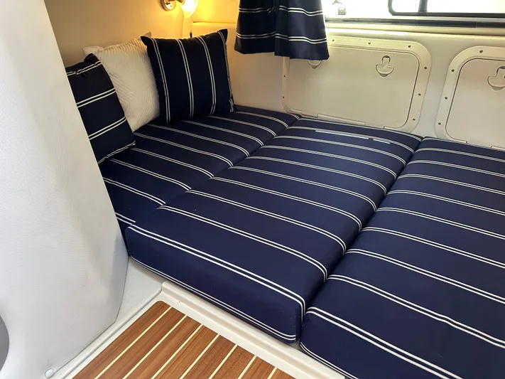 Last One II Yacht Photos Pics 2015 Wellcraft 290 Coastal cabin with striped navy cushions and wooden flooring.